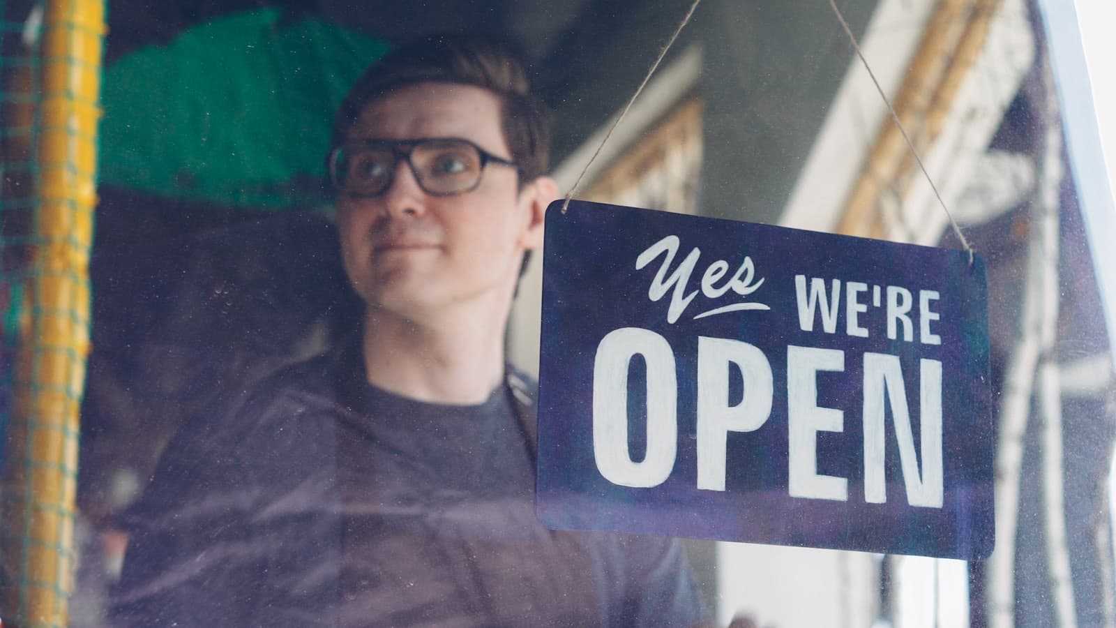 Shop owner behind an open sign in the window of an established business