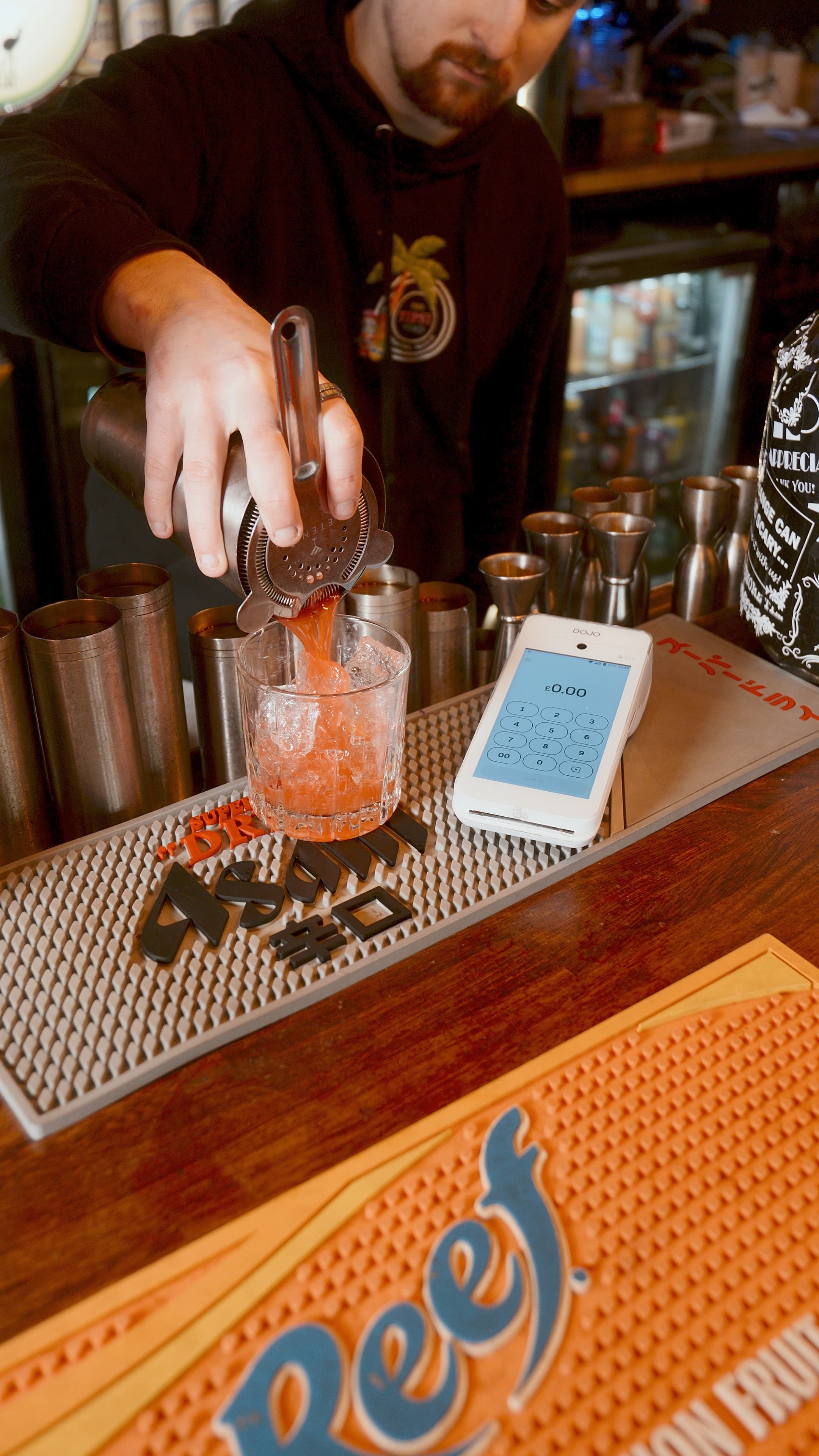 Bartender pouring cocktails with a Dojo terminal on the bar