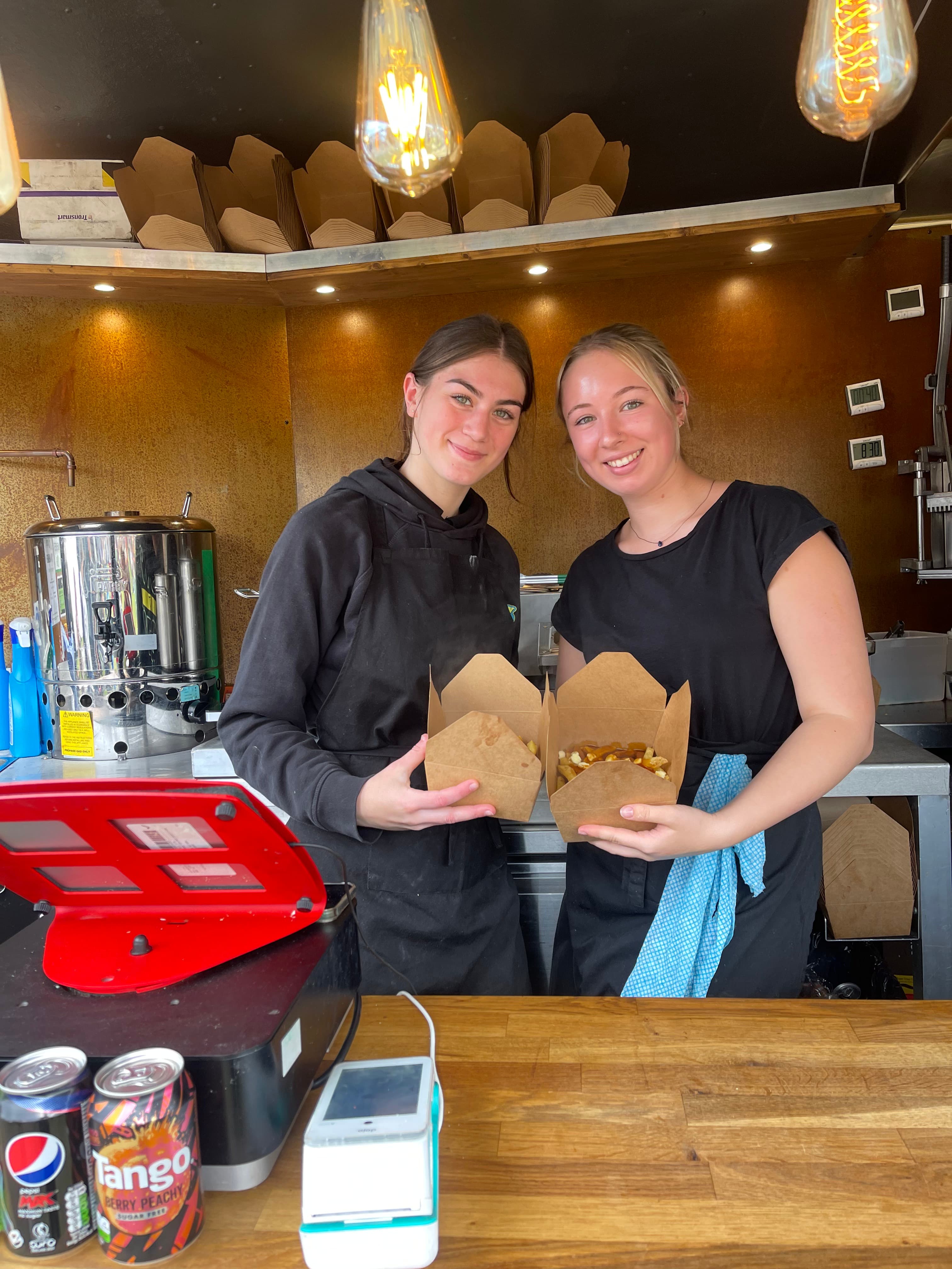 Two staff members holding food boxes at the counter of one of our takeaway clients, card reader on the counter