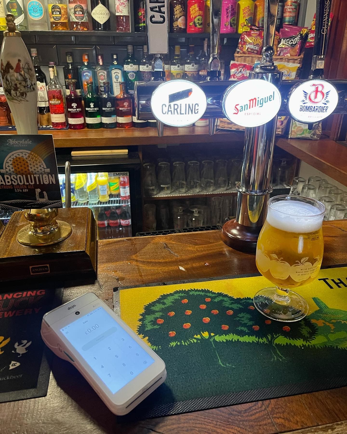 Dojo terminal on a pub bar beside a freshly poured pint, with beer pumps behind